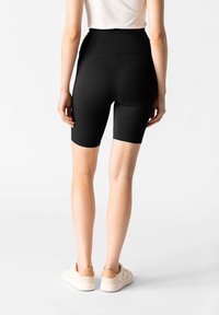 Shorts neri a vita alta realizzati in tessuto elastico, caratterizzati da una texture liscia e una forma aderente, abbinati a sneakers chiare.