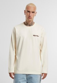 Crème lange mouw t-shirt van zacht katoen met een ronde hals, voorzien van een bruin bedrukt logo op de linkerborst en een relaxed fit.