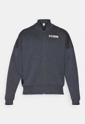 Sweatshirt zippé gris foncé avec des poignets et un ourlet côtelés, arborant "FCBM" en texte blanc sur la partie gauche de la poitrine et une poche latérale.