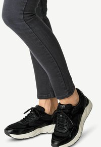 Schwarze Sportschuhe mit einer strukturierten Oberseite, Schnürdesign und einer weißen Sohle. Schlanke graue Jeans mit einer enganliegenden Silhouette.