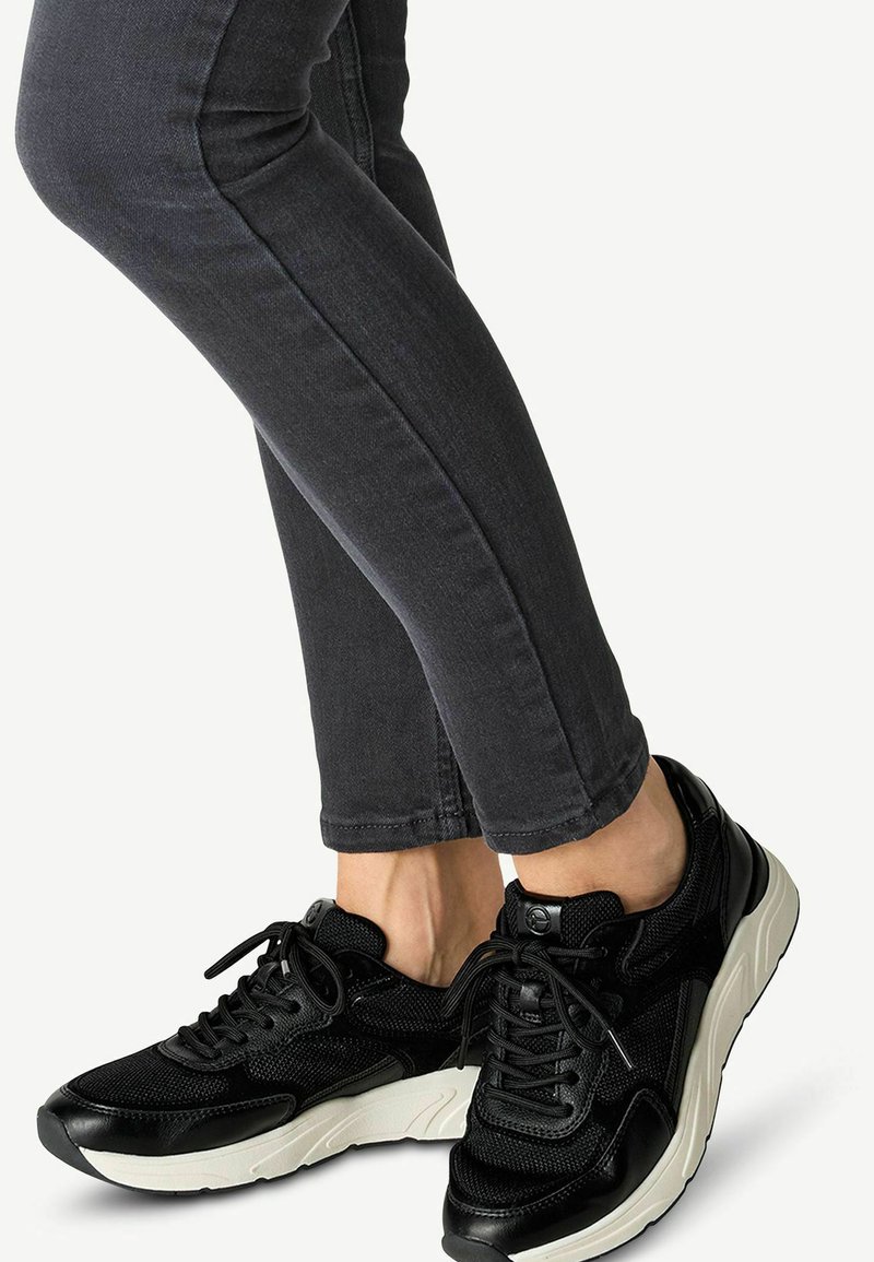 Schwarze Sportschuhe mit einer strukturierten Oberseite, Schnürdesign und einer weißen Sohle. Schlanke graue Jeans mit einer enganliegenden Silhouette.