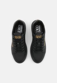 Svarta lädersneakers med rund tå, platt sula, snörning, med guld-logotyp på utsidorna och tryckt varumärkesnamn inuti.