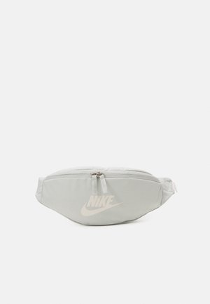 Lichtgrijze Nike heuptas met ritssluiting en verstelbare band, met een wit Nike-logo aan de voorkant.