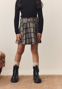Black ribbed long-sleeve top with a pleated green and black plaid skirt, accented by a belt. Paired with chunky black boots and beige socks.