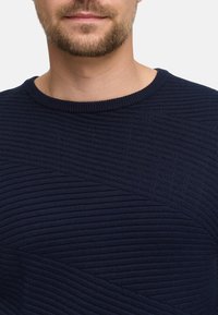 Mørkeblå strikkegenser med en teksturert, ribbestruktur med horisontale linjer, rund hals og uten synlige lukkinger eller detaljer.