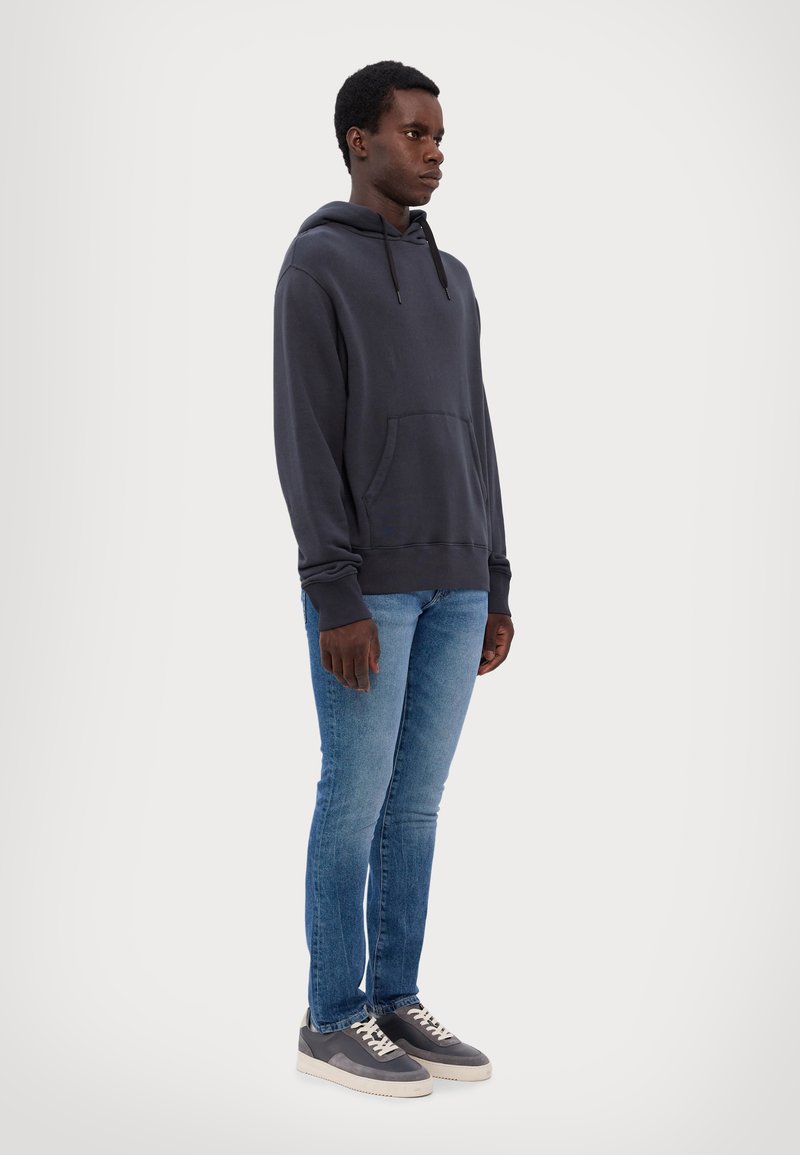 Mørk grå hettegenser med frontlomme, kombinert med lyseblå slim-fit jeans og grå sneakers med hvite såler. Enkel design, myk tekstur.
