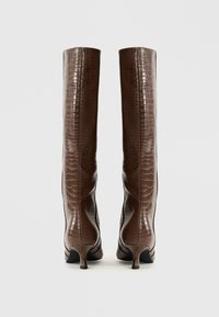 Bottes montantes en fausse cuir embossé crocodile marron avec une silhouette incurvée et des talons effilés. Texture lisse, sans quincaillerie visible.