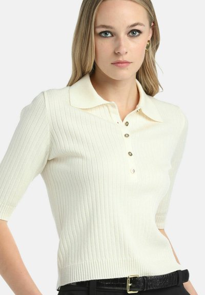 Hladký krémový polo tričko s krátkymi rukávmi, obsahujúce preložený golier a zapínanie na tri gombíky. Stylizované s čiernym opaskom.