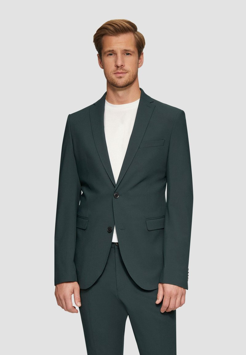 Dunkelgrüner maßgeschneiderter Blazer mit schlanker Passform, einreihiger Knopfverschluss, eingelegten Revers und zwei Vordertaschen. Kombiniert mit einem weißen Hemd.