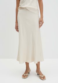 Light beige, satin midi skirt with a flared shape, featuring smooth texture and subtle draping detail at the waist. Worn with simple sandals.
