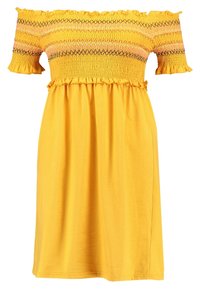 Žluté šaty s volnými rameny, zdobené smocks tělem, volánovými rukávy a sukní do kolen vyrobenou z měkké tkaniny.