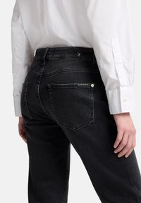 Czarne dżinsy z denimu z pięcioma kieszeniami, dopasowanym krojem i subtelnymi przeszyciami. Na tylnej części pasa znajduje się mała metka z logo marki.