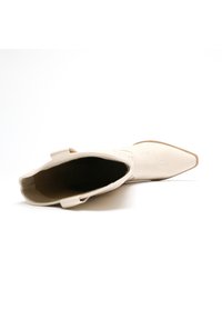 Botas vaqueras de punta afilada en cuero beige, con costuras decorativas y dos lengüetas para facilitar su puesta. Textura suave con diseño minimalista.