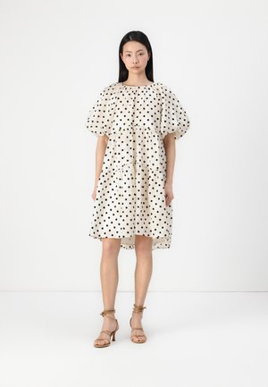 Cream dress with black polka dots, short puff sleeves, gathered waist, and a flared silhouette, paired with beige strappy heels.