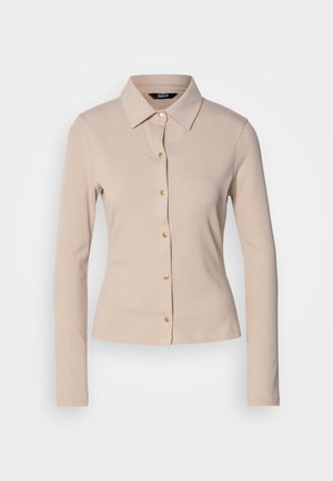 Chemise à manches longues beige en ribbed avec un col et des boutons à l'avant. Présente une coupe ajustée et une texture subtile.