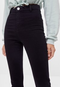 Högmidjade svarta jeans i denim, med knäppning fram och fickor, med en figurnära silhuett och slät yta.