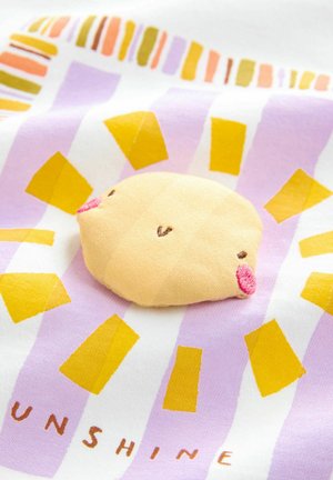 Žuti plišasti oblik sunca s izvezenim facialnim značajkama, postavljen na ljubičastu i bijelu tkaninu s šarenim zrakama sunca i tekstom.