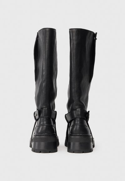 Μαύρες δερμάτινες μπότες μέχρι το γόνατο με απαλή υφή, φαρδύ κουντεπί, διακοσμητικές αγκράφες και χοντρή σόλα. Φερμουάρ στην εσωτερική πλευρά.