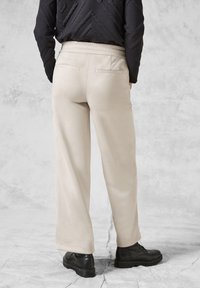 Beige brede bukser lavet af blødt stof, med et flad-front design og elastisk talje, parret med sorte snørebåndssko.