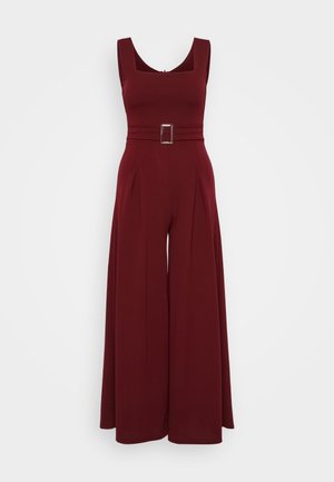Bordó overall, négyzet alakú dekoltázzsal, széles lábú kialakítással, plisszírozott részletekkel és ezüst színű, téglalap alakú csattal a derékon.