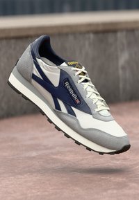 Retro Reebok tenisice s gornjim dijelom od bijelog i sivog nubuka, mornarsko plavim akcentima, teksturiranim dizajnom i bijelim vezicama, s podstavljenim ovratnikom i detaljem s logom.