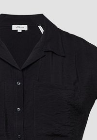 Zwarte shirt met korte mouwen van gekreukt stof, met een kraag, knoopsluiting aan de voorkant en twee opgestikte zakken.