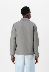 Grå jacka med en avslappnad passform, med krage och elastiska muddar, kombinerad med ljusblå jeans. Slät tygkänsla.