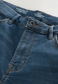 Jeans de mezclilla azul oscuro con un ajuste relajado, que presentan costuras visibles, un botón de metal y una cintura elástica cómoda.