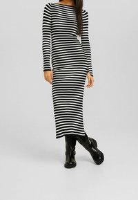 Abito a righe bianco e nero, a coste, con maniche lunghe, forma aderente e spacco laterale, abbinato a stivali neri al ginocchio.