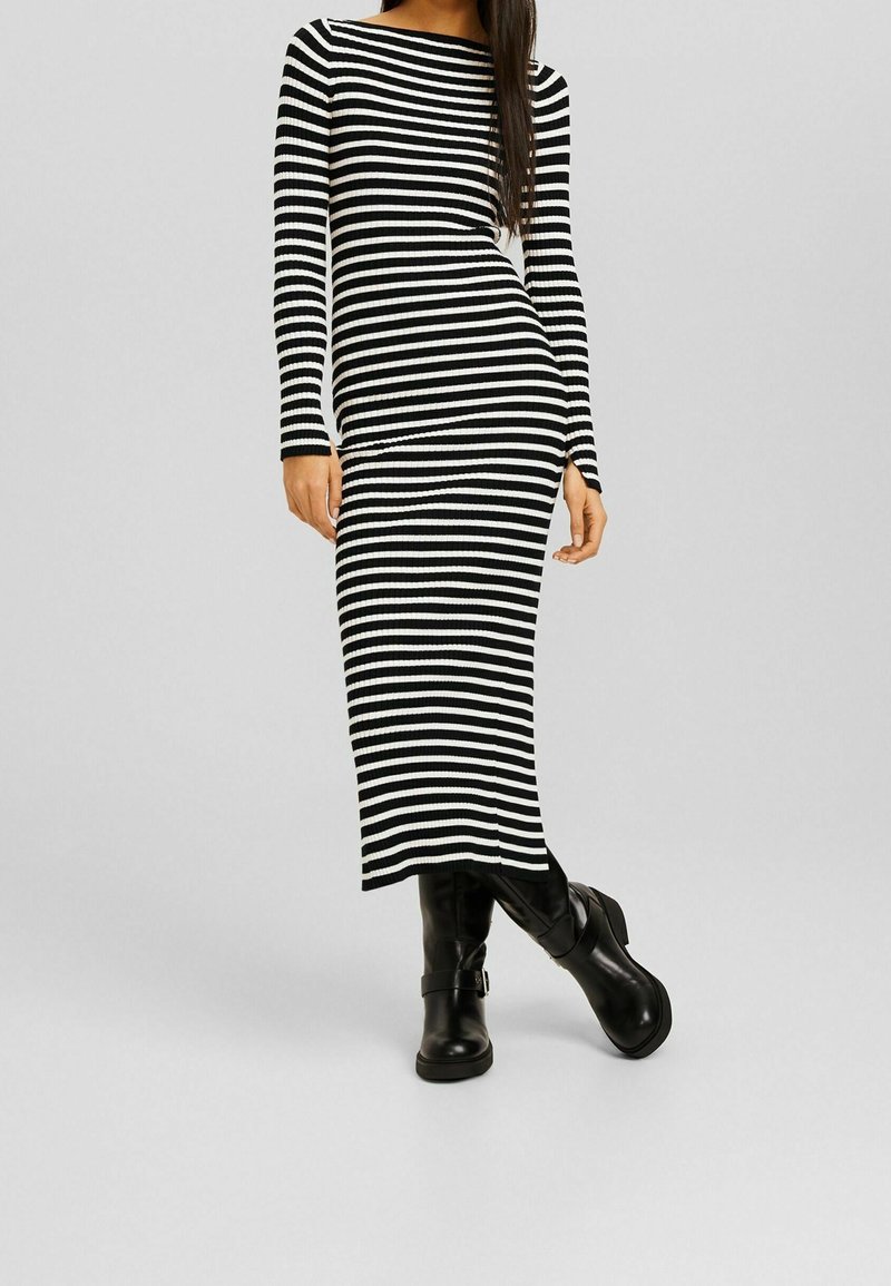 Abito a righe bianco e nero, a coste, con maniche lunghe, forma aderente e spacco laterale, abbinato a stivali neri al ginocchio.