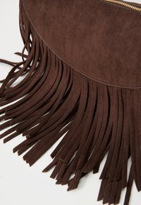 Borsa in suede marrone con lunghi accenti frangiati lungo il fondo, dotata di una parte superiore liscia e una chiusura a zip. Design testurizzato e alla moda.