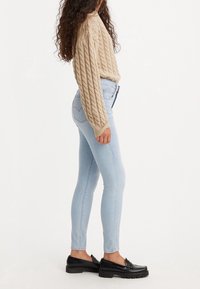 Jersey de punto beige, jeans ajustados azul claro y zapatos mocasines negros, mostrando una textura de tela y un diseño ajustado.