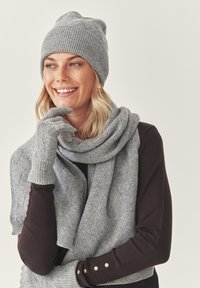 Grijze gebreide beanie, sjaal en handschoenen. De beanie heeft een geribbelde textuur, de sjaal heeft een ruitpatroon, en de handschoenen hebben een strakke pasvorm met geribde manchetten.