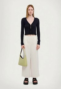 Marineblå rillet crop cardigan, brede hvide bukser og sorte platformsandaler. Holder en lille lys grøn håndtaske med en rem.