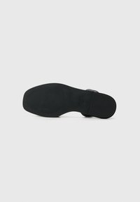 Platt svart sandal sula med gummimaterial, texturerade räfflor för grepp och en minimalistisk design. Ingen synlig märkning på hälen.
