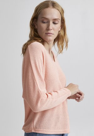 Lichtroze, loszittende trui met lange mouwen, V-hals en zachte, gestructureerde stof. Subtiel patroon overal, gecombineerd met denim.