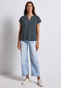 Short-sleeve, V-neck top in dark teal with a textured pattern, paired with light blue wide-leg jeans and white sneakers.