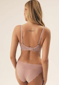 Jasnoróżowy koronkowy biustonosz z regulowanymi ramiączkami i zapięciem na hak, w połączeniu z pasującymi bezszwowymi majtkami o wysokim stanie z falbaniastym wykończeniem.