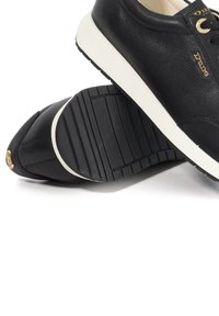 Pair of black leather sneakers with white soles and gold branded accents, one shoe showing its grooved black rubber sole.