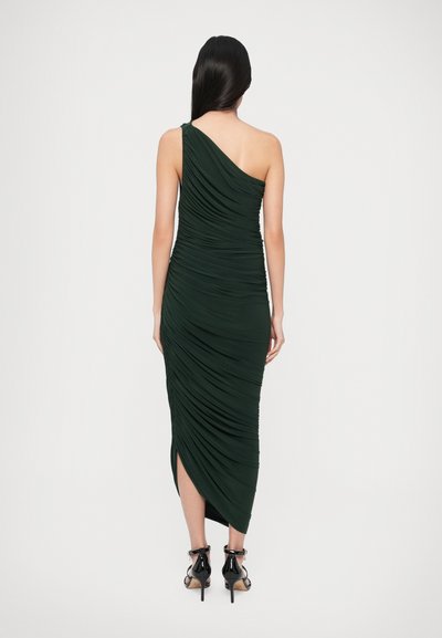 Zelené šaty na jedno rameno s našuchoreným efektom a bočným rozparkom, s hladkým materiálom a priliehavým strihom, doplnené čiernymi remienkovými sandálmi.