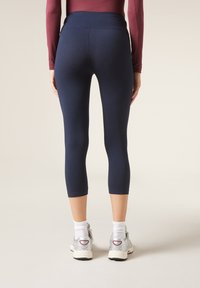 Leggings capri en color navy con una cinturilla ancha, textura suave, ajuste ceñido y un dobladillo por encima del tobillo, combinados con zapatos deportivos plateados.