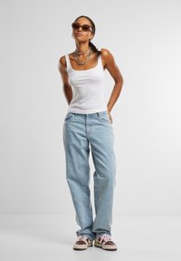 Un débardeur blanc, un jean bleu clair ample et des baskets marron avec des lacets roses. Comprend des lunettes de soleil et des colliers en métal superposés.