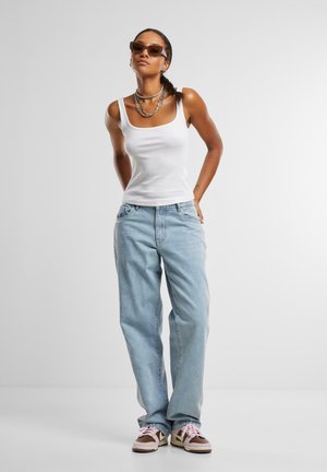 White tank top, light blue loose-fitting jeans, and brown sneakers with pink laces. Includes sunglasses and layered metal necklaces.