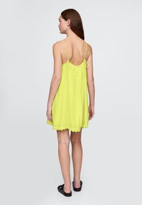 Obleka brez rokavov v svetlo rumeni barvi, ohlapnega kroja, z nazobčenim robom in detajlom z gumbi na zadnji strani. Mehka tkanina z lahkotno teksturo.