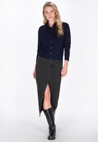 Navy knitted cardigan with a bow tie detail, paired with a black denim skirt featuring a front slit, and knee-high black boots.
