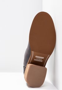Zapato de gamuza gris con una suela de goma marrón texturizada. Presenta un diseño cosido y un detalle del logo en la plantilla. Perfil de tacón plano.