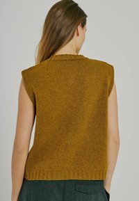 Top senza maniche di colore senape in maglia, con scollo e orlo a costine. Texture morbida, vestibilità leggermente ampia e design minimalista.
