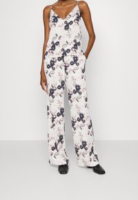 Ensemble de tissu léger à motif floral comprenant un haut sans manches à col en V et un pantalon à jambe large. La palette de couleurs inclut un rose doux et des accents sombres.