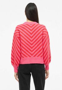 Pull rose présentant un motif en chevrons avec des nuances variées, manches longues bouffantes, col rond et ourlet côtelé.