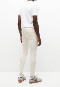 Pantalones crema ajustados con una textura suave, que cuentan con dos bolsillos traseros y una cinturilla de altura media, combinados con una camiseta blanca y zapatillas deportivas.